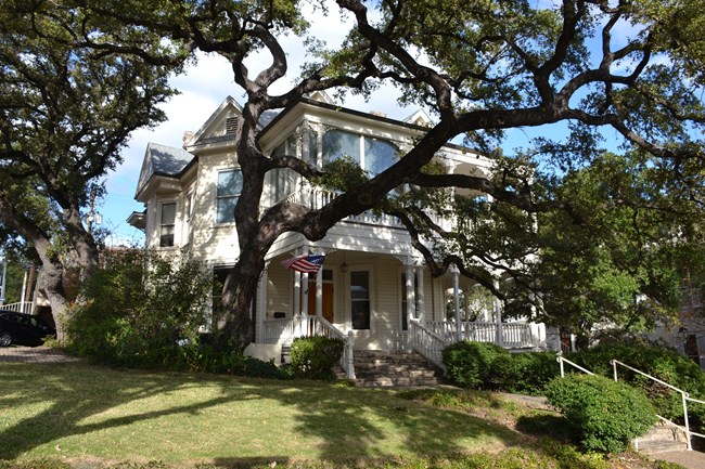 Two story white, Queen Anne style house with front yard.