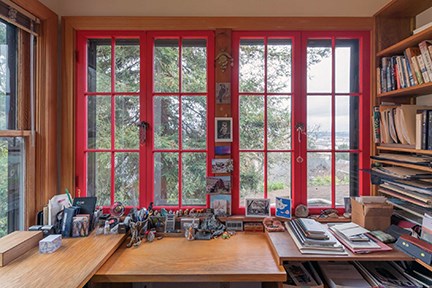 Interior of a home showing a view through windows with red frames. A bookshelf sits at right.
