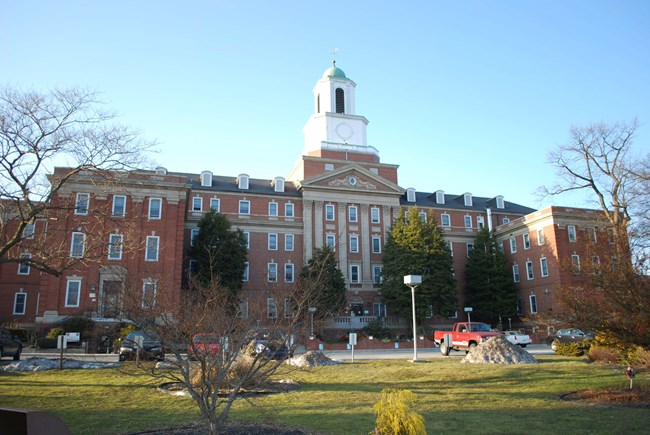 Large four-story nineteen bay, hip-roof building with a flat-roof central projecting pavilion. A copper-domed cupola is located above the building's central block.