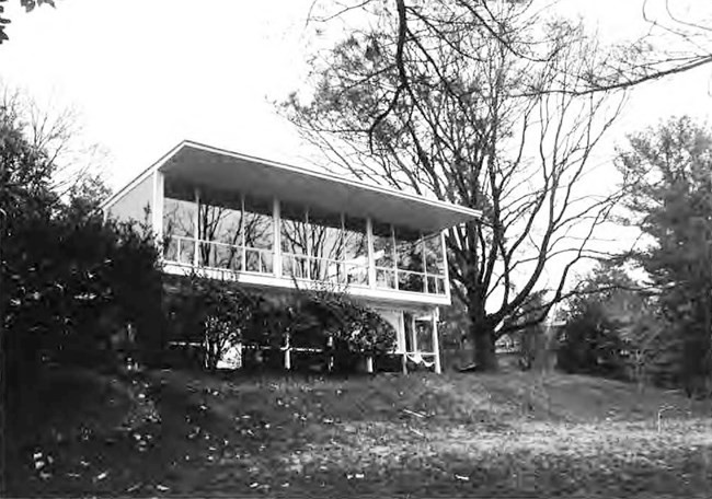 Modern two-story house with large windows set within a landscape of lawn and trees.