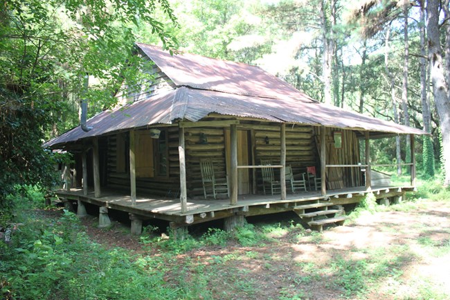 Log cabin with wrap-around porch set in woods