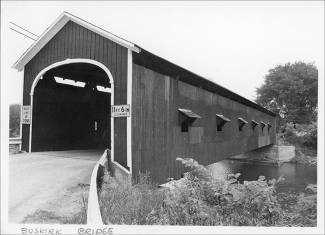 78003457 Buskirk Covered Bridge Image of wooden covered bridge, road, and water.