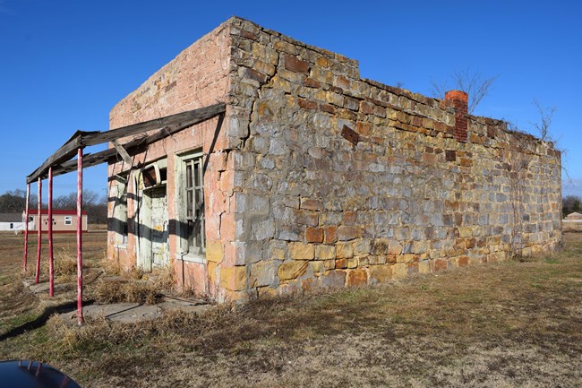 Image of single story brick building with porch, grass, and sky.