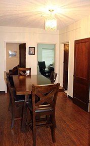 View of a room with white walls, several doors, and a wooden table surrounded by wooden chairs.