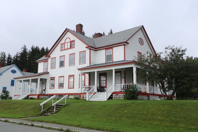 Three-story structure with a large peaked roof, white siding, and red trim.