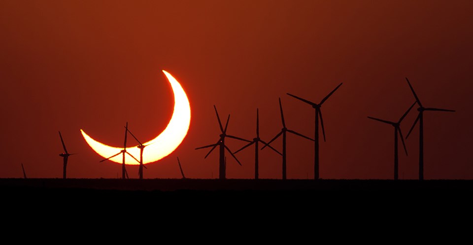 Crescent eclipse behind windmills