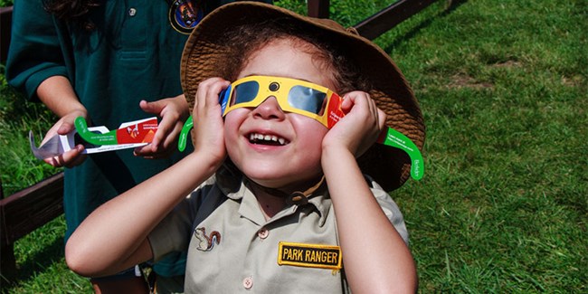 a child smiles toward the sun wearing eclipse safety glasses