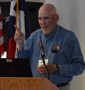 Bald white man in blue shirt with the NPS Arrowhead standing behind a podium.