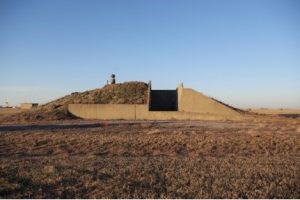 Ammunitions Magazine #129 A low cement dome half covered in grass with a large rectangular opening right of center.