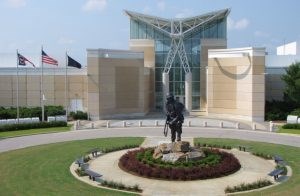 Museum entrance 15-foot-tall statue of a soldier stands in front of the entrance to tan building. Three flags on poles on the left.