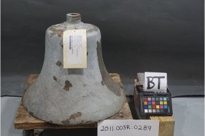 Bell A large weathered bell with tag sits on a wooden pallet with a sign reading 2001.003R.00289. A second sign reads B T.