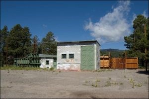 Gray cinderblock shed with numbers reading 516 and two tall green doors with other smaller structures behind it.