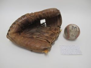 A well-used old baseball-mit, weather baseball with the letter M, and a 3 by 5 index card with a handwritten note.