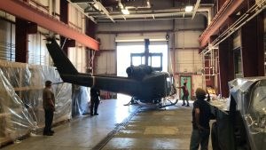 UH-1B Huey Helicopter Four people standing inside a large building as the rotor-less UH-1B Huey helicopter is being moved.