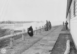 Five men gray uniforms one with letters PW on back of shirt building a thick rail fence.