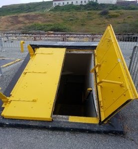 Two bright yellow steel magazine doors one open the other closed are the angled entry to stairs leading underground.