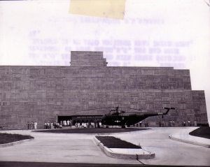 A helicopter sits in front of a multi-story wide rectangular building with a geometric façade.