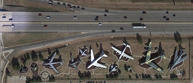 Aerial view looking down on 11 different modern aircraft next to a busy interstate highway.