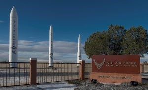 Three white missiles stand behind near a sign reading US Air Force F.E. Warren Air Force Base. Home of the Missileer.