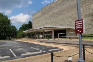 Building 54 Parking lot and entrance to a multi-story wide rectangular building with a geometric façade.