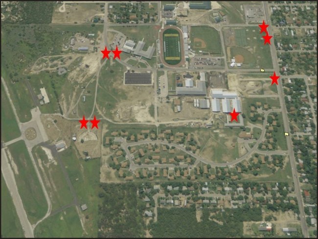 Eight red stars on aerial photo of small city. Houses at bottom, and larger buildings and athletic fields in center.