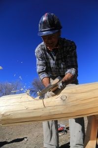 A man wearing a hardhat using an axe to carve a notch in a log.