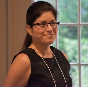 Woman long black hair pulled back and glasses wearing a sleeveless black top.