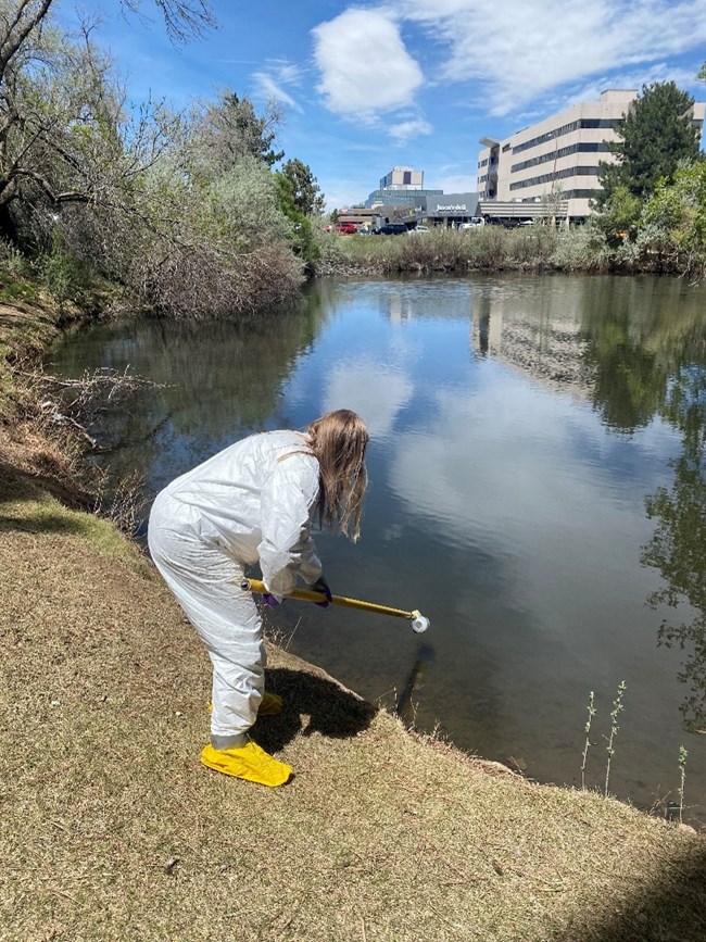 PPE during Oil Spill Response Training A person with long blond hair wearing a white Tyvek suit, shoes coverings and gloves as they clean up oil spilled in a river.