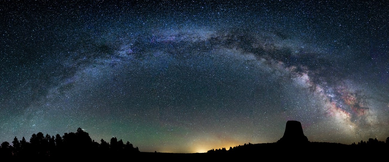 the milky way stretches across the night sky with silhouettes of rocky outcrops