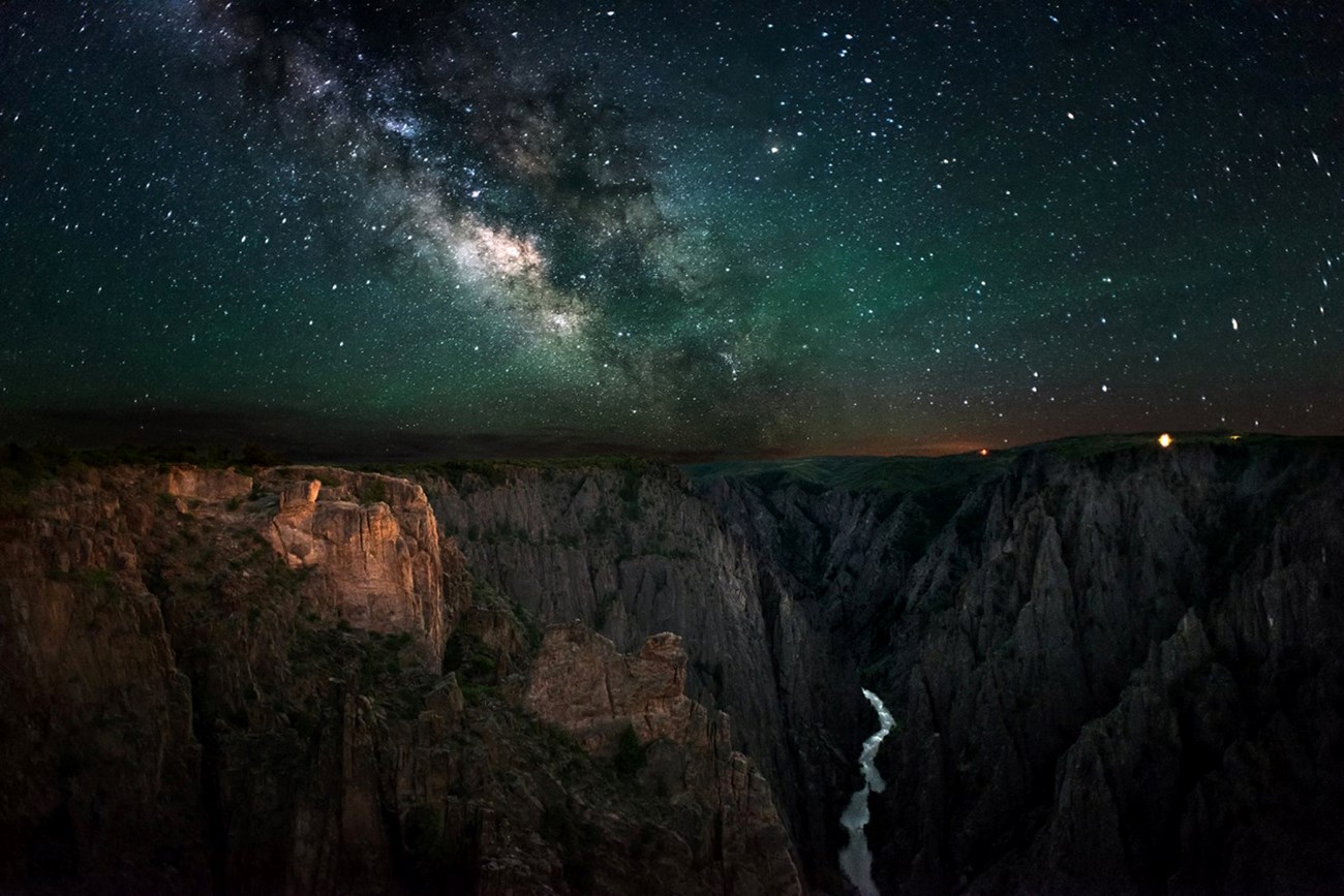 black canyon night skies A star-filled night sky frames this dramatic view of rocky cliffs and gorge at Black Canyon of the Gunnison National Park, Colorado.