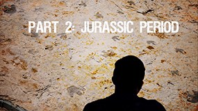 a rock wall with a silhouette of a person in front. a roaring t rex skull and the words Part 2 Jurassic Period on it