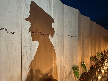 Shadow on a memorial wall lined with flowers