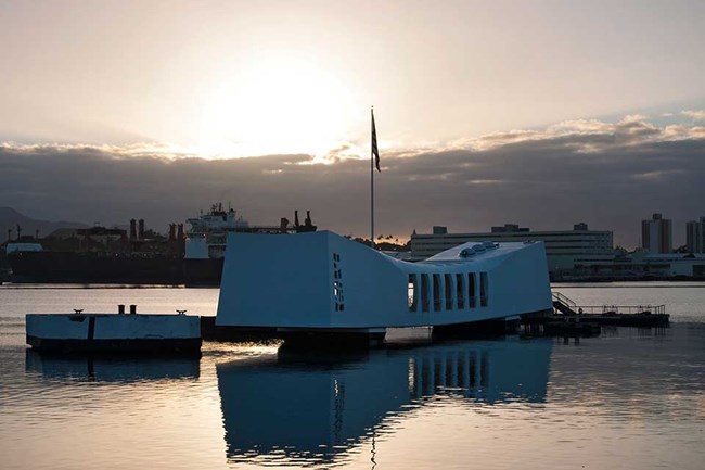 white memorial structure suspended above ocean water with city skyline in background