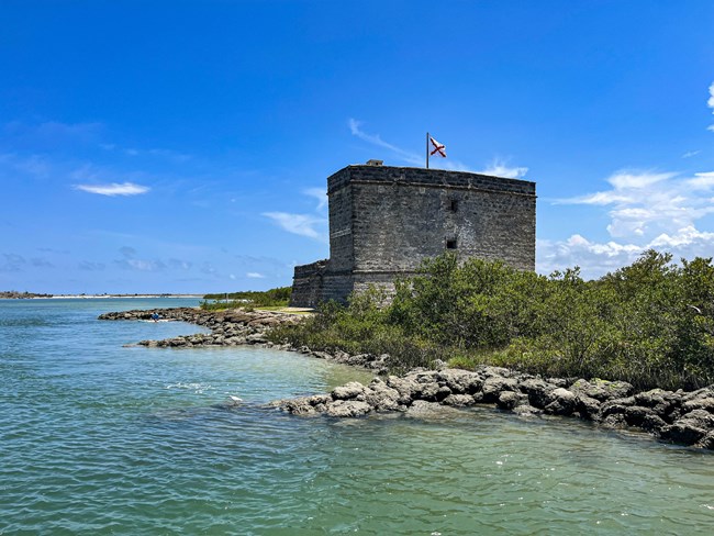 Small two-story stone Spanish colonial fort on an island with a rocky shore and wetlands