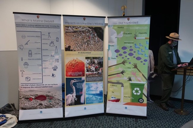 Three pop up banners highlighting issues with marine debris stand next to a park ranger in a conference room