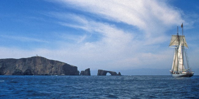 Sail boat with island and clouds in the background.