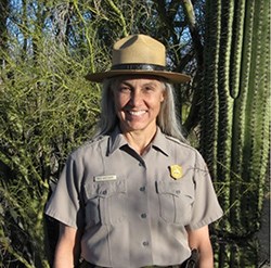 Meg Weesner in NPS uniform stands in front of a cactus and other desert vegetation.