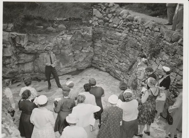 Black and white photo of a group of people in a quarry listening to a park ranger