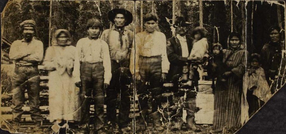 A creased and aged photo of a row of people posing in Alaska, ranging in age.