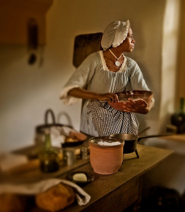 Ajena Rogers stands in a kitchen holding a mixing bowl during costumed interpretation in character as Hannah