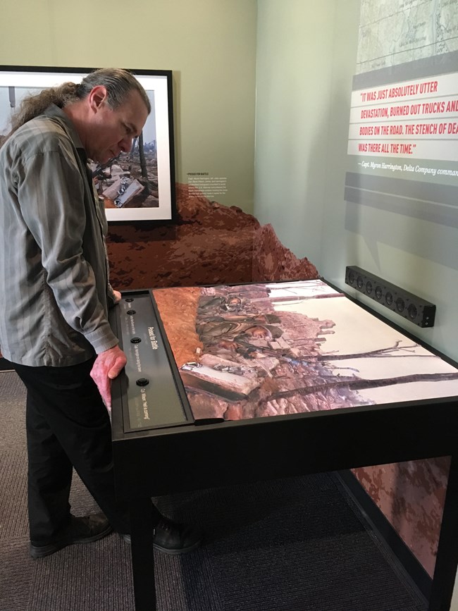 Ray Bloomer leans over a battlefield map exhibit that includes visual images and buttons for audio description.