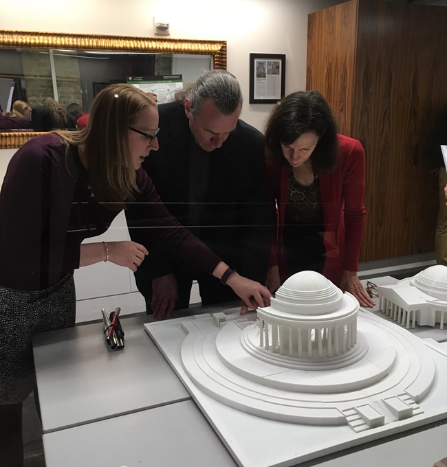 Ray Bloomer standing between two people, leans over a table where there is a three-dimensional model of the Jefferson Memorial, a round building circled by columns.
