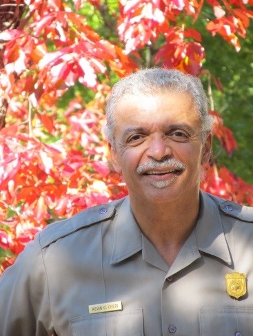 Kevin Cheri, in NPS uniform, in front of a backdrop of fall leaves