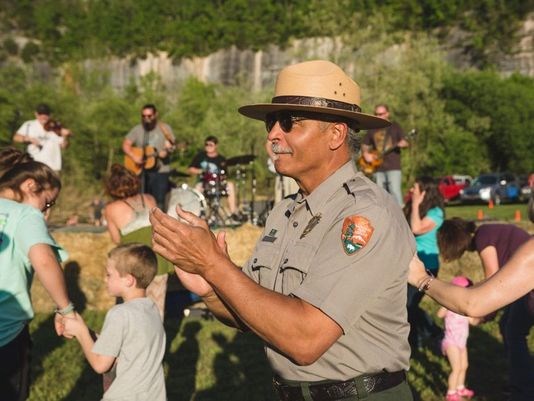 Kevin Cheri, in NPS uniform, clapping, among a crowd of people watching a band play in an outdoor setting