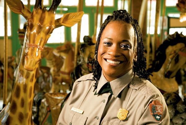 An NPS ranger in uniform, an African American woman, beside on the the animal seats inside a carousel