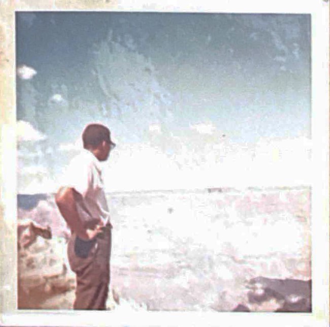 1960s photo of James Etheredge, a young African American man with glasses, stand with hands on hips and looks over the Grand Canyon.