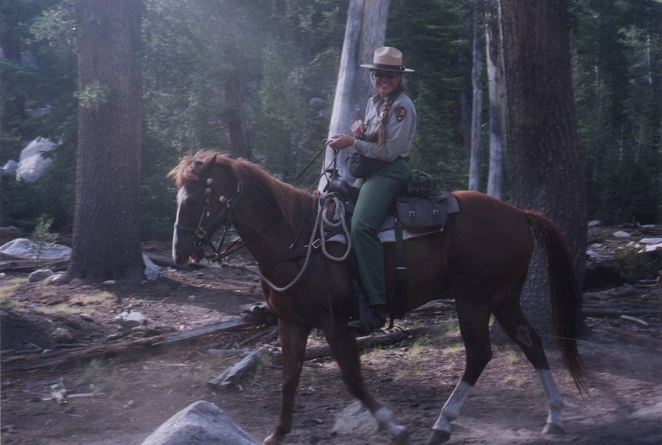 Laurel Boyers on horseback surrounded by trees, wearing National Park Service uniform