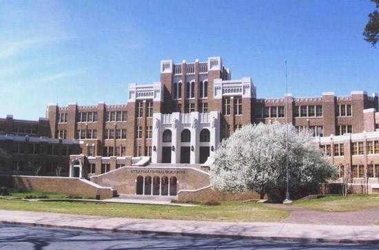 Facade of a large symmetrical brick school with a staircase leading to the towering entryway