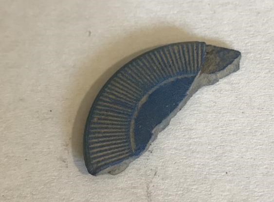A section of a broken poker chip has a pattern of ridges around the edge.
