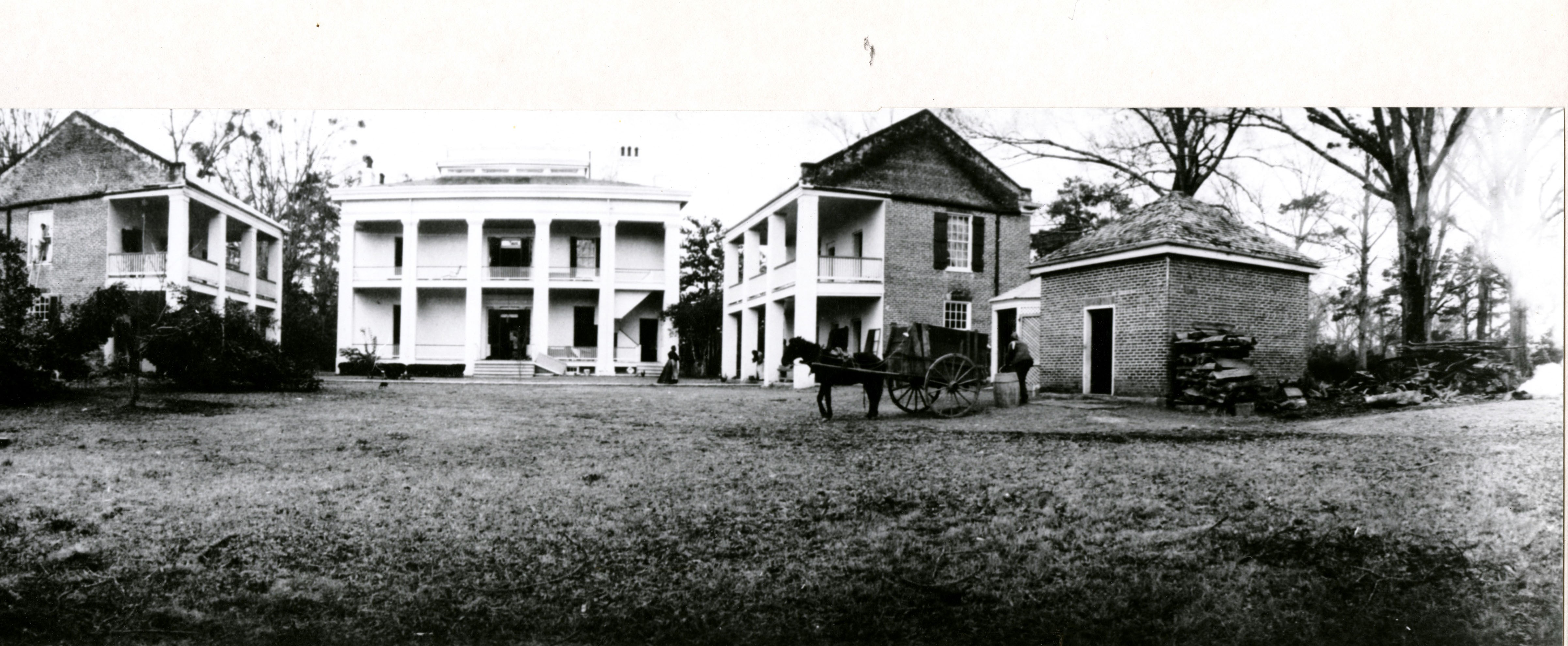 Three large, two-story structures with columns and porches are arranged to form a courtyard. A horse and carriage stand in the yard.